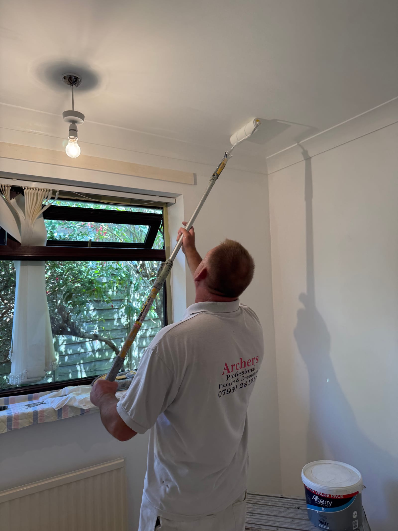 An Archers decorator in branded workwear rolling a freshly painted ceiling